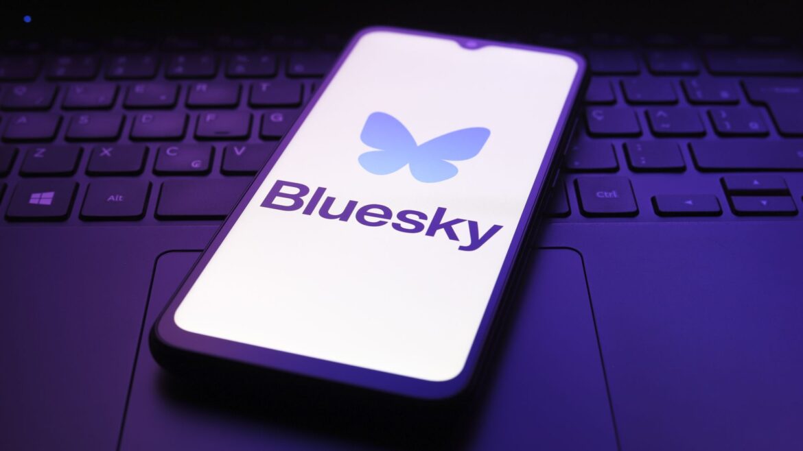 The Bluesky app logo appears on the screen of a smartphone lying on a laptop keyboard