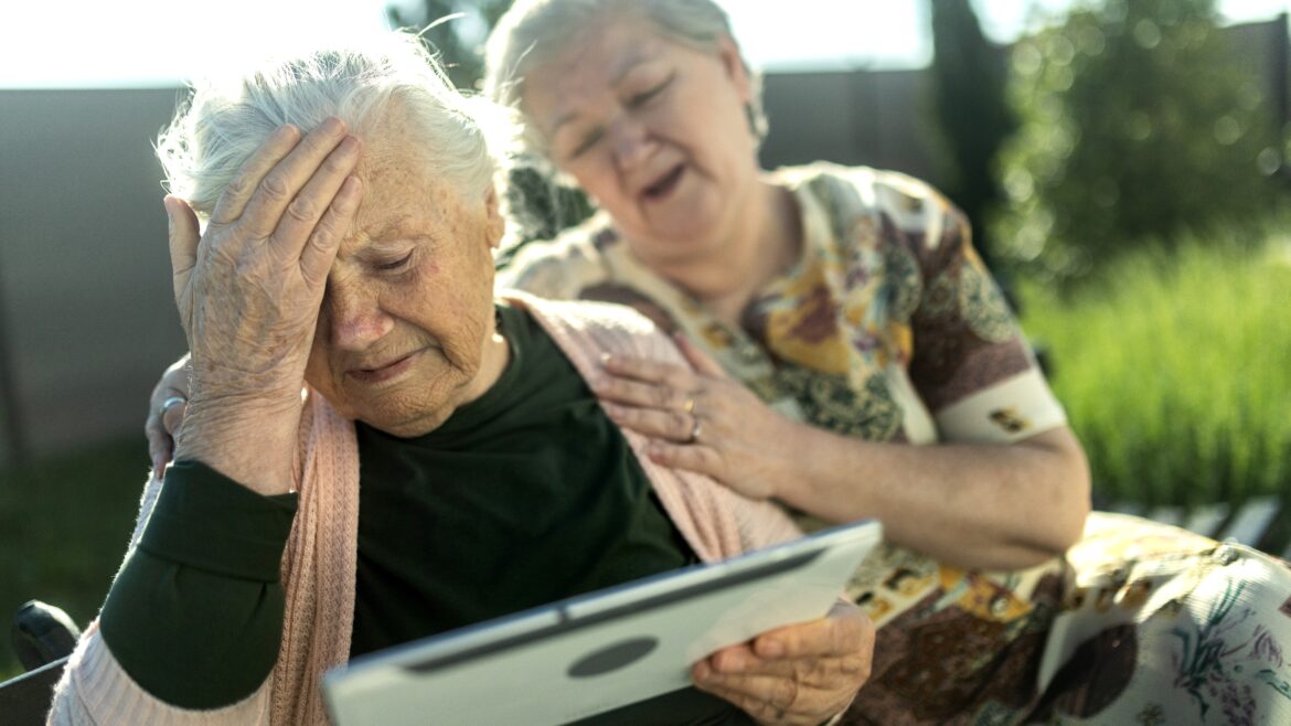 An elderly sad woman in a wheelchair looks at a tablet and talks to her family via video call - stock photo